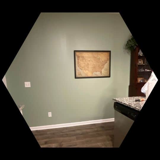 Green-painted kitchen wall with framed map art, granite countertops, and hardwood flooring.