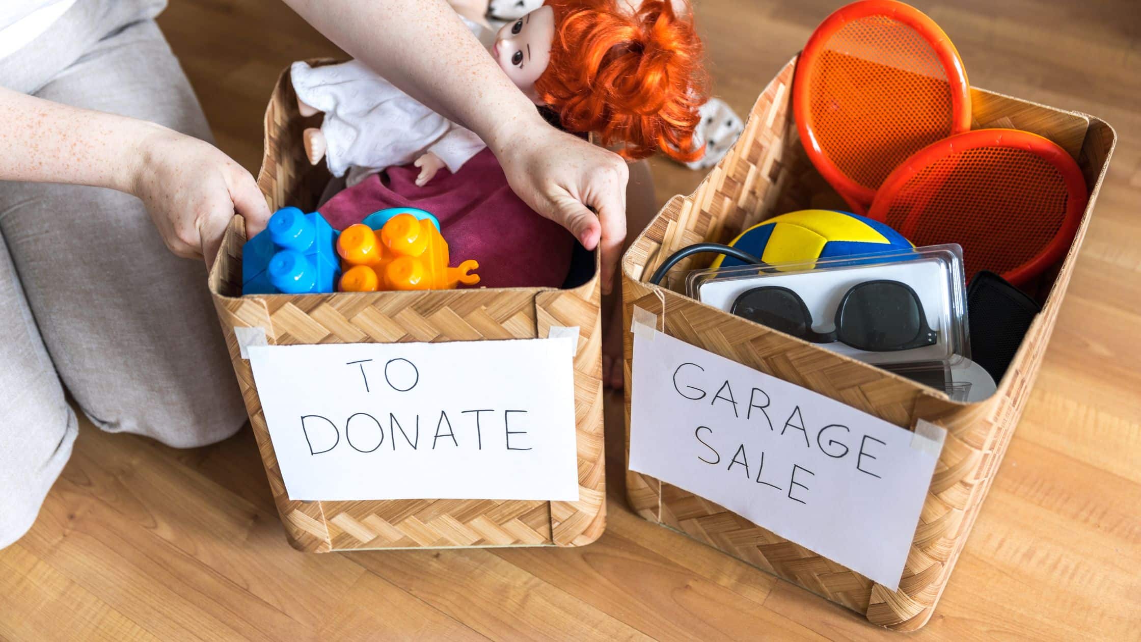 Person sorting items into labeled baskets for donations and a garage sale, featuring toys, clothes, and household items.